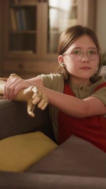 Kafkasyalı sakin bir kızın dikey portresi gözlüklü ve kol protezi ile rahat oturma odasında oturuyor ve kameraya bakıyor.