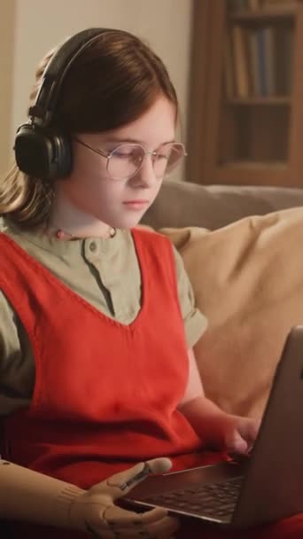 白人家庭女学生带着仿生臂 戴眼镜和耳机在家里上网学习的垂直侧影 — 图库视频影像