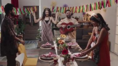 Cinco de Mayo partisinde dört mutlu erkek ve kadının renkli aile evinde gitar çalıp, şarkı söyleyerek, marakalarla dans ederek şenlikli yemek masasının önünde tam bir yakınlaştırma çekimi.