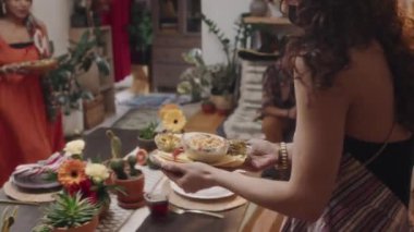 Genç İspanyol kadının çiçek ve kaktüslü güzel yemek masasına tako, nachos ve guacamole taşırken arkadaşlarıyla ev partisine hazırlandığı orta boy yakın çekim görüntüleri.