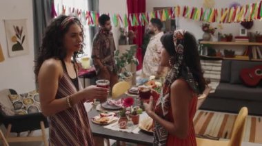 Parlak başörtüsü takmış iki Meksikalı kız, Cinco de Mayo partisinde sohbet ederken, güzel dekore edilmiş bir evde, ellerinde margarita tutarken, kadeh tokuştururken ve tokuştururken.