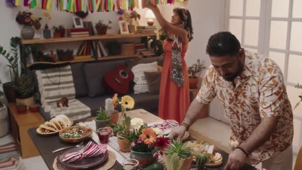 墨西哥年轻夫妇准备家庭聚会 把食物放在桌上 挂花环 朋友们端着菠萝和龙舌兰 拥抱和亲吻 — 图库视频影像