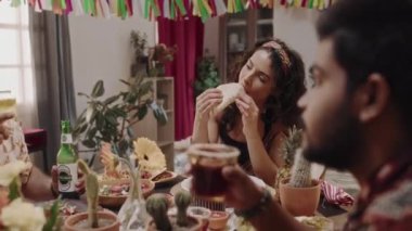 Cinco de Mayo 'yu kutlarken bir grup Meksikalı' nın ziyafetin tadını çıkardığı orta boy bir fotoğraf. Bira ve kokteyl içen iki adam, bir şeyler tartışıyor, kadın chalupa yiyor ve dinliyor.