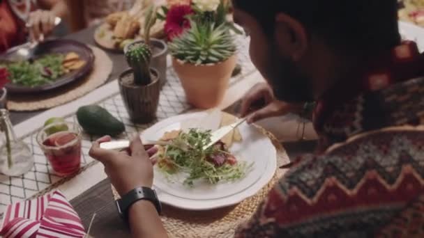 在派对上与朋友一起坐在桌旁 享用着美味的传统食物晚餐 用刀叉吃着沙拉的拉美裔男子的高角镜头 — 图库视频影像