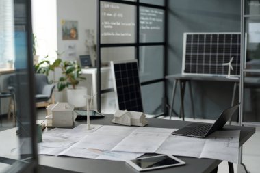 Dijital tabletler, dizüstü bilgisayarlar, ev modelleri ve modern mimarın işyerindeki yel değirmenleriyle çevrili taslaklar.