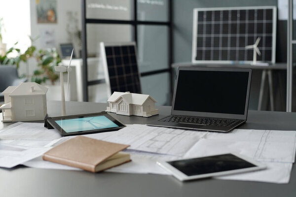 Часть просторного офиса с рабочим местом архитектора, работающего над новым проектом с использованием мобильных гаджетов, эскизов чертежей и макетов