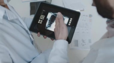 Tanımlanamayan beyaz önlüklü erkek ve kadın doktorların dijital tabletteki göğüs boşluğunun röntgen taramasına bakıp anormallikleri göstererek teşhis konularını tartışarak yakın plan çekimleri.