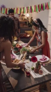 İki genç Meksikalı ya da İspanyol kadının ulusal bayramı kutlamak ve sohbet etmek için sofraya kızarmış mısır, nachos, salsa, guacamole koyduğu orta boy dikey bir fotoğraf.