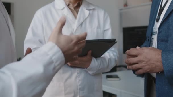 身着西服 身穿白衣的医生站在办公室 就某件事达成一致并握手 背景为平板电脑的女同事的中等特写镜头 — 图库视频影像