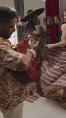 Meksika şapkalı bir Meksikalı 'nın dikey görüntüsü. Marakas ve gitarda halk şarkısı çalan bir arkadaşı. Cinco de Mayo' da dans eden, kıvrımlı, çiçekli genç bir kadın.