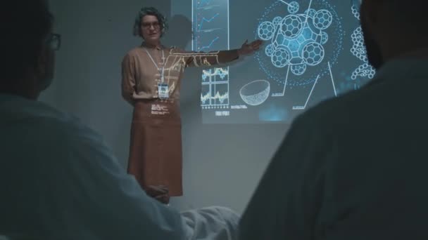 部门会议上 中年白种人女医生站在放映机屏幕旁边 与同事们谈论新的疗法 新疗法的作用和效果 — 图库视频影像