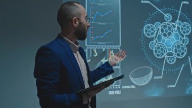 Orta büyüklükte gözlüklü bir Orta Doğulu adam görüntüsü. Konferansta sahnede projektör ekranında duruyor. Biyokimya veya farmakoloji üzerine bilimsel araştırmalar hakkında konuşuyor.