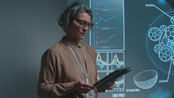 白种人女科学家或教授的中肖像画 带着平板电脑和耳机 站在放映机屏幕旁边 讲授生物化学 转向相机 微笑着 — 图库视频影像