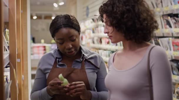 中年非洲裔美国人销售助理向白人女性顾客推荐新的面部血清 讲述其成分和好处 同时在化妆品商店工作 — 图库视频影像