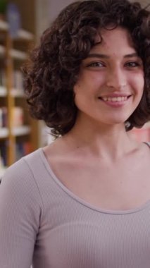 Mağazanın önünde kozmetik ve makyajla kameraya gülümseyen kıvırcık kumral saçlı güzel beyaz bir kadının orta boy dikey portresi.