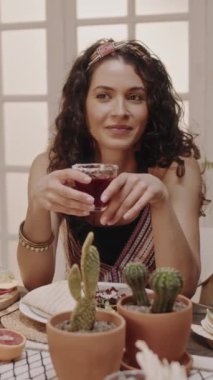 Siyah dalgalı saçlı, saç bandı takmış, elinde margarita kokteyli olan ve arkadaşlarıyla sohbet eden Latin bir kadının orta boy dikey görüntüleri.