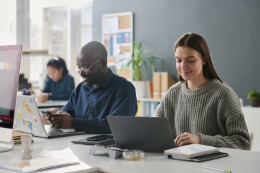 Modern ofisteki iş yerinde dizüstü bilgisayarlar ve akıllı telefonlar üzerinde çalışan genç erkek ve kadın uzmanlar seçici odaklanma, kopyalama alanı