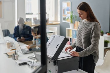 Ofiste çalışan beyaz bir kadın, arka planda akıllı telefonları kullanan Asyalı ve Siyahi meslektaşları...