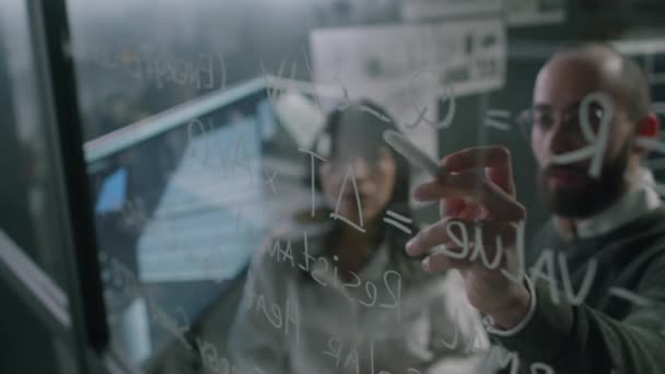 男性と女性の代替エネルギー専門家のガラス映像を通じて オフィスの新しい低炭素技術をエンジニアリングしながら数式で作業する — ストック動画