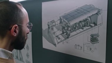 Gözlüklü erkek mühendisin, temiz enerji departmanında çalışırken işletim süreçlerini geliştirirken duvara yapışan yel değirmeni motor planıyla ilgili notlar alırken görüntülerini çıkar.