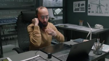 Çift taraflı yenilenebilir enerji tasarrufu CEO 'sunun bilgisayarda çalışırken telefonla konuştuğu ve modern ofiste grafik tablet kullanırken gece duvarlarında planlar olduğu orta büyüklükte görüntüler.