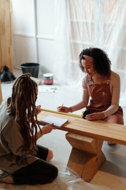 İki genç tasarımcı ya da girişimci kafenin önünde oturmuş, tadilat sırasında ahşap tezgah ölçüleri alıyorlar.