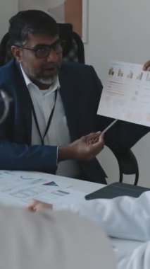 Hint hastane yöneticisinin başhekim ve başhekim ile birlikte ofiste otururken çekilmiş orta boy dikey görüntüsü yönetim toplantısında karlılığı artırmanın yollarını öneriyor.
