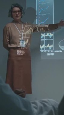 Personel toplantısında projektör ekranının yanında duran olgun beyaz kadın CEO 'nun tam dikey görüntüsü. Yıllık sonuçlar hakkında doktorlara konuşuyor, slaytlardaki grafiklere ve istatistiklere işaret ediyor.