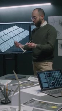 Erkek alternatif enerji uzmanının dikey tam görüntüsü ofiste yapılan iş konferansında yeni rüzgar türbininin pervanelerini prototip kulesine sabitlemesini açıklıyor.