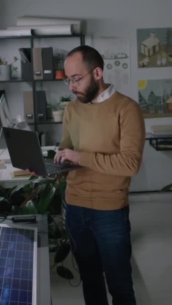 阁楼办公室工作期间 男性太阳能工程师站在太阳能电池板碎片附近 在笔记本电脑上快速输入信息和特征的垂直侧面完整的介质画面 — 图库视频影像