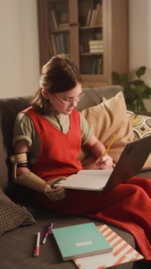 Protez eğitimi alan, not tutan ve dizüstü bilgisayardan online ders ya da eğitim videosu izleyen beyaz öğrencinin dikey görüntüleri.