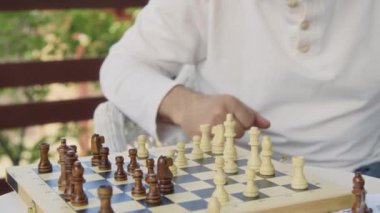 Yazın açık havada oturan, satranç oynayan, hareket eden ve rakip taşları yakalayan orta yaşlı iki adamın yakın çekim görüntüleri.