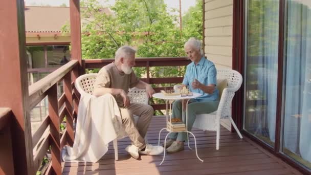 在阳光明媚的夏日 白种人老年夫妇坐在乡间露台上的扶手椅上 玩国际象棋 放松身心 — 图库视频影像