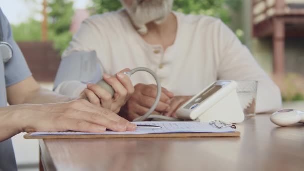 隐姓埋名 手持袖口监测器的老年男性患者 在退休机构工作时 身着制服 无法辨认的女性医务工作者手部中弹 为他们测量血压 — 图库视频影像
