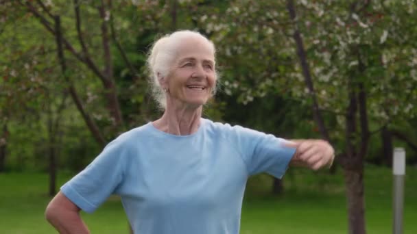 健康とフィットネスを維持しながら ウエスト回転と腕延長演習を行い グループ内の公園に立っている青色のコカシア人女性の笑顔のミディアムクローズアップ肖像画 — ストック動画