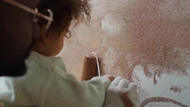 手で赤ん坊を抱え 部屋の改造中にローラーを使用して彼女の絵の壁を助ける介護の父親の肩のクローズアップ — ストック動画