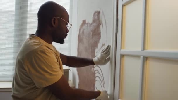 黑人男子在今后的托儿所做彩绘工作时 在门口贴上遮羞布带的侧斜镜头 婴儿帮他 用迷你滚筒粉刷墙壁 — 图库视频影像