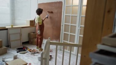 Bekar bir annenin hamilelik döneminin sonlarına doğru duvarları kahverengiyle boyarken gelecekteki çocuklar için odaları yeniden dekore ederken çekilmiş tam görüntüleri.