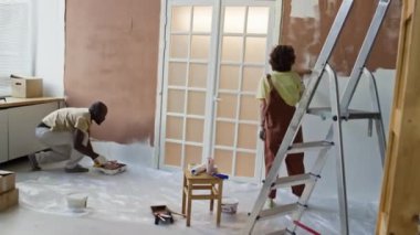 Yeni dairenin yenilenme işlemi sırasında duvarları kahverengi boya ve fırça ile boyayan karı-koca görüntülerinin tam görüntüsü.