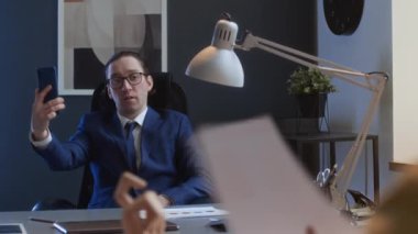 Narsist beyaz erkek şirket yöneticisinin orta omuz üstü fotoğrafı. Masa başında oturmuş, video görüşmesi yapıyor, kendine hayran oluyor, zorbalık yapıyor ve astlarına sataşıyor.
