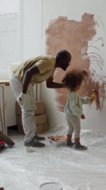 Küçük kızıyla duvarları kahverengiye boyarken bekar bir babanın çocuk odasını yeniden dekore edişinin dikey görüntüsü.
