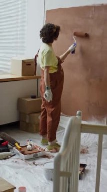 Bekar bir annenin hamilelik döneminin sonlarına doğru, duvarları kahverengiyle boyarken, müstakbel çocuk için odaları yeniden dekore ederken çekilmiş dikey görüntüleri.