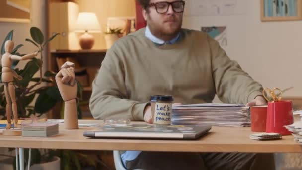 中等比例的红头发白种人男性上班族坐在办公桌前 手里拿着一叠文件 找到了外卖咖啡 上面写着求和 喝酒和敬酒的字条 — 图库视频影像