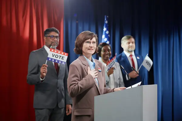 成熟的微笑女人手挽手 看着选民 站在讲台上 用话筒说话 — 图库照片