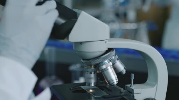 생화학 실험을 수행하는 슬라이드의 시료에서 현미경으로 피어싱하는 연구원의 얼굴의 클로즈업 — 비디오