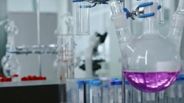 Yakın çekimde, kimya laboratuarında duran mor kimyasal sıvıyla cam tepkimeye maruz kalan hiç kimse, test tüpleri, arka planda mikroskop...