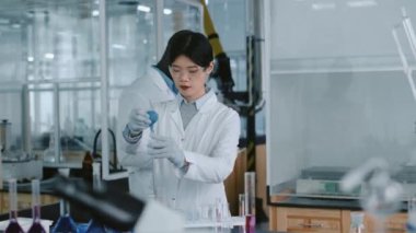 Çinli araştırmacının deney tüpüne ampul pipetli reaktör eklediği orta boy bir fotoğraf. Tabletli Afrikalı Amerikalı erkek meslektaşı deney sonucunu yaklaşıp paylaşıyor.