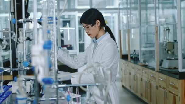 中国女科学家白衣 护目镜 手套在药瓶中加入试剂滴滴 检查反应或残留的中等镜头 同时进行测试 — 图库视频影像