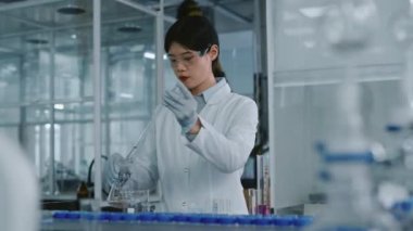 Genç Çinli kadın laboratuvar çalışanı, temiz çözeltiyle pembe kimyasal maddeyi şişeye boşaltıp dairesel hareketlerle karıştırırken,