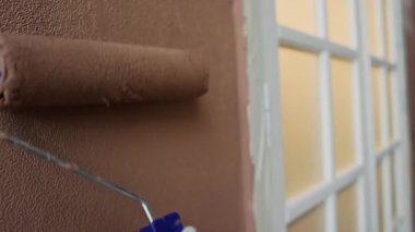 Ciddi bir Afro-Amerikalı adamın yakın plan fotoğrafı. Evdeki duvar süslemesi. Karısıyla birlikte odayı boyarken boya silindiri kullanıyor.